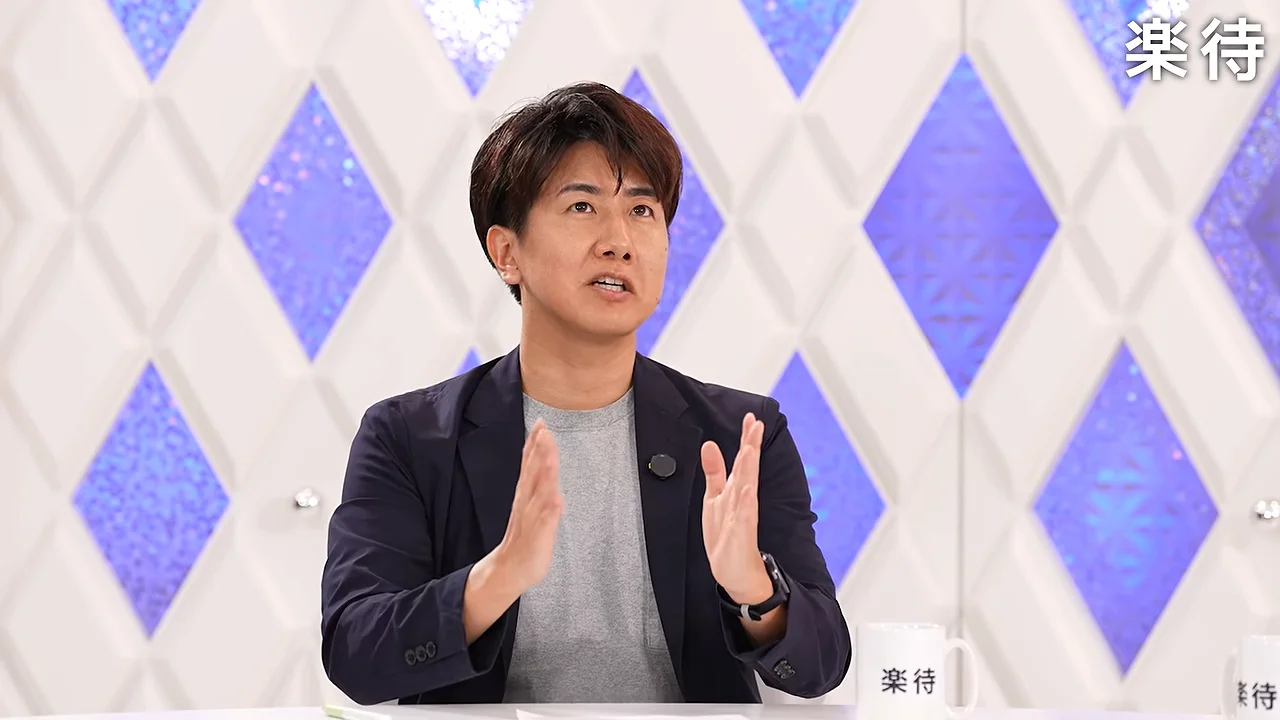 紺色のジャケットを着た男性が身振りを交えて話している様子。