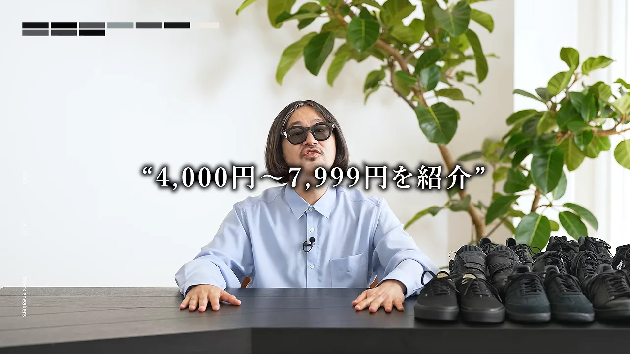黒いスニーカーが並んだテーブルの前で、サングラスをかけた男性が話しています。