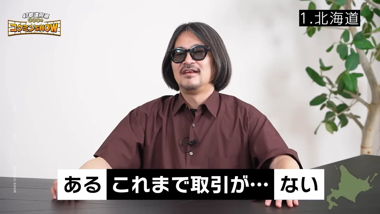 机の前に座り、カメラに向かって話すサングラスをかけた男性