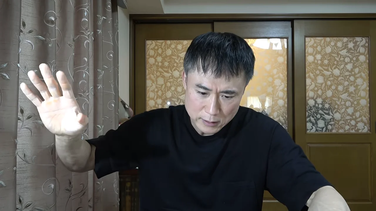 男性が右手を掲げながらカメラに向かって真剣な表情で話しています。