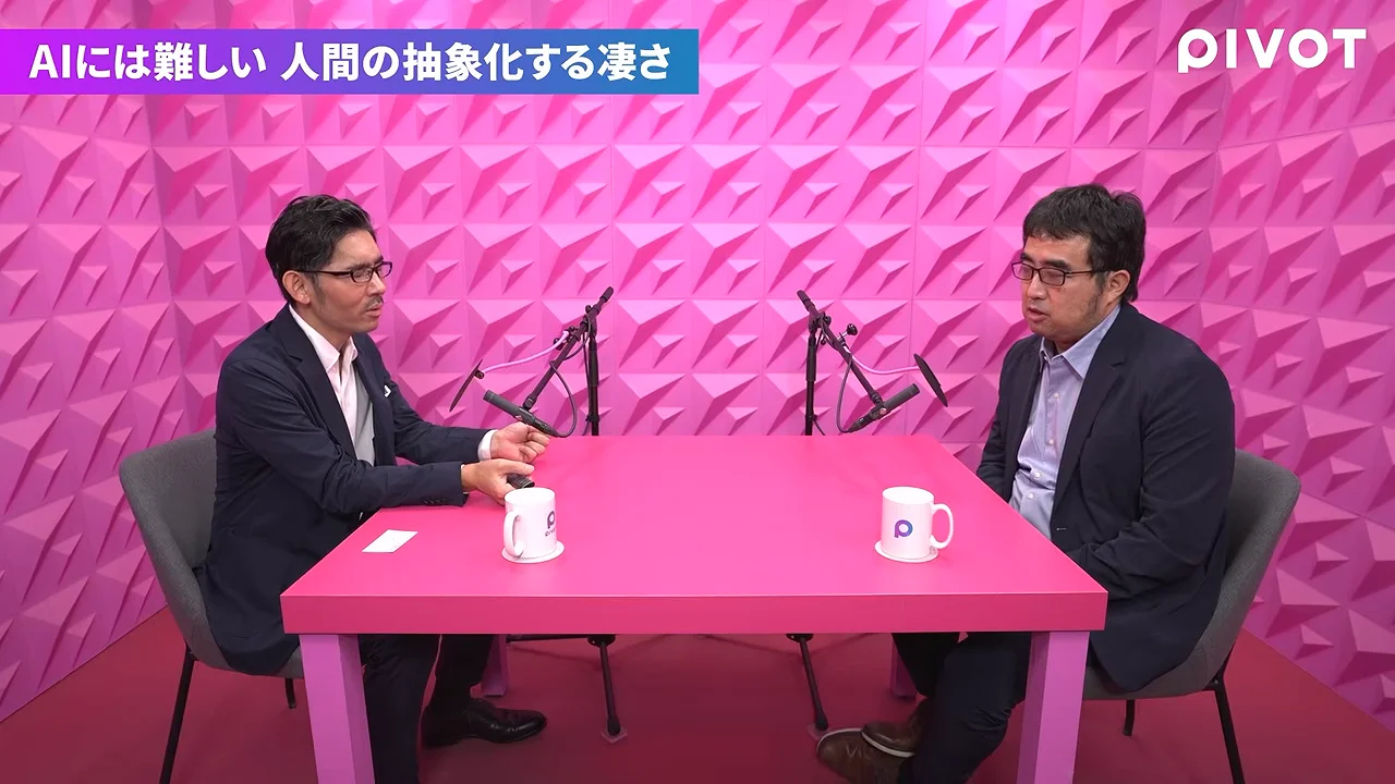 ピンク色のスタジオで、2人の男性がピンクのテーブルを挟んで向かい合って座っています。