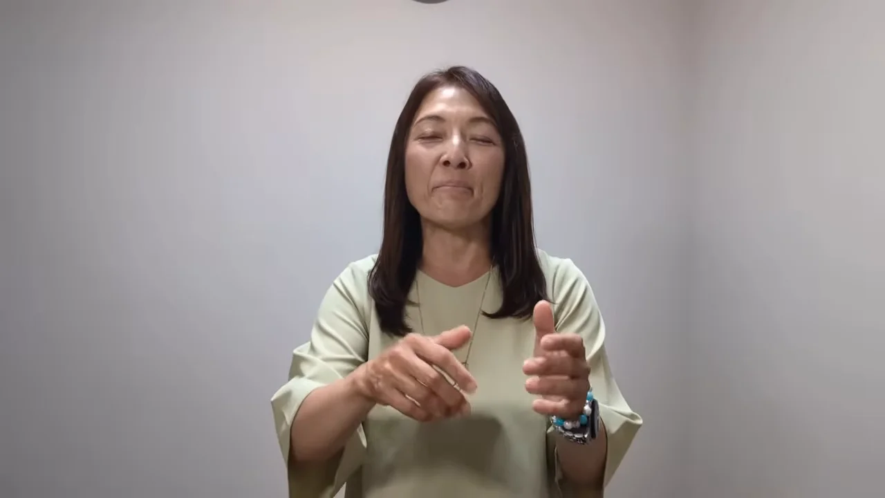 白い壁を背景に、両手を前に出して話す女性