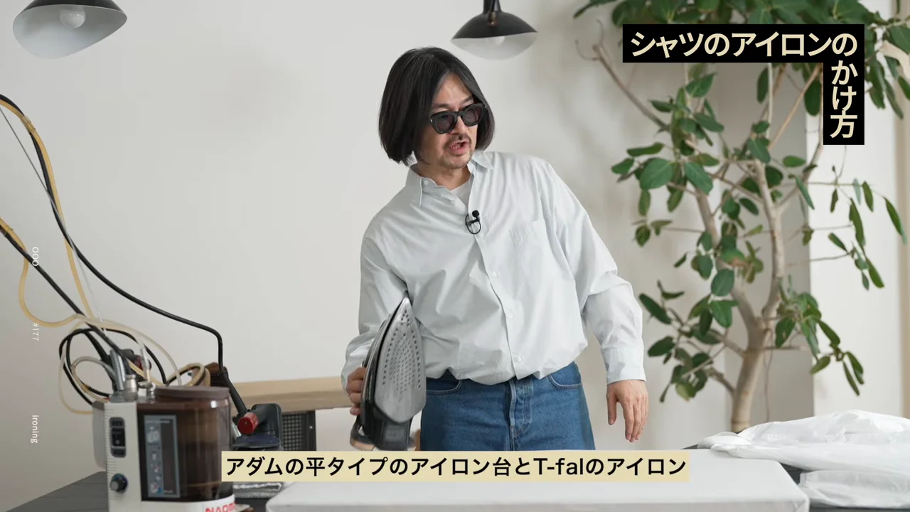 男性がアイロンを片手に持ち、アイロン台の前に立っています。