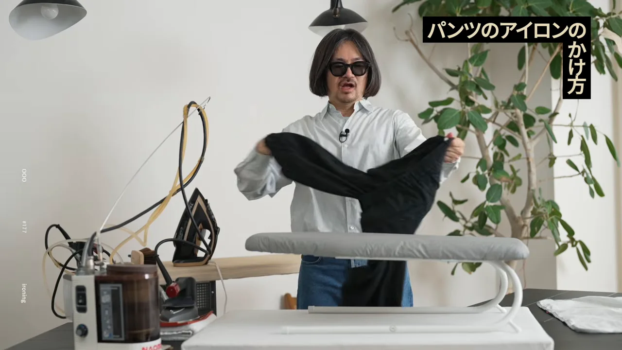 男性が黒いパンツを両手で持ち、アイロン台の前に立っています。