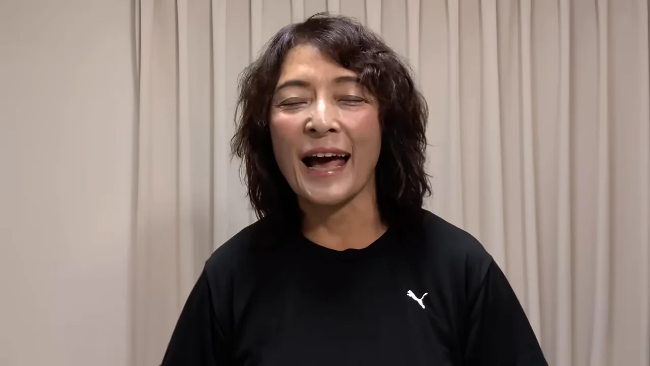 黒いTシャツを着た女性がカーテンの前で正面を向いて話しています。