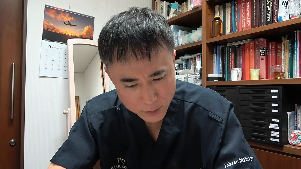本棚を背にした黒い服の男性が下を向きながら話しています。