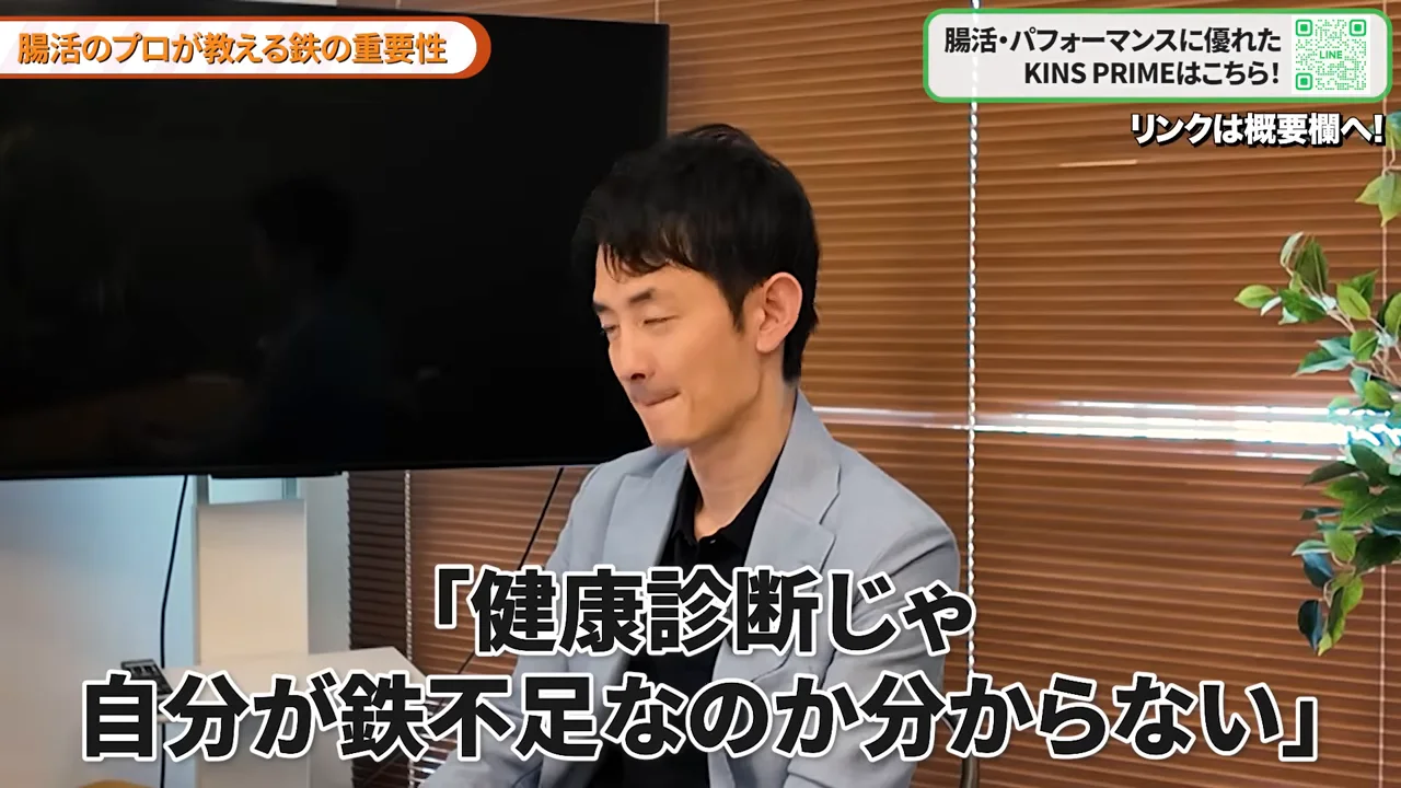 ブラインドの前で水色のジャケットを着た男性が話している様子