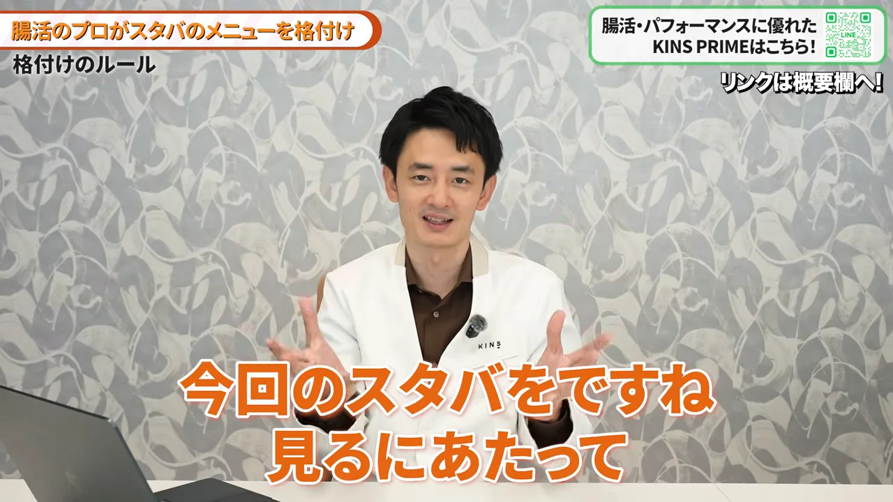 白衣を着た男性が両手を広げてカメラに向かって語りかけている様子