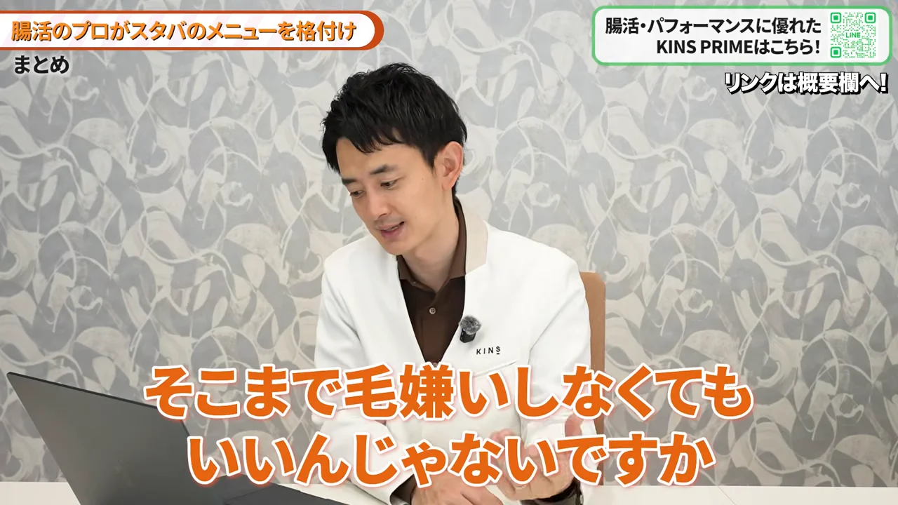 白衣を着た男性がノートパソコンの置かれた机の前で下を向きながら話している様子