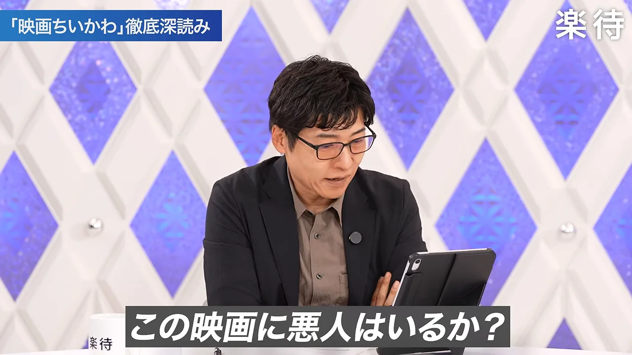 スタジオでタブレットを見つめながら話す眼鏡をかけた男性のアップ。