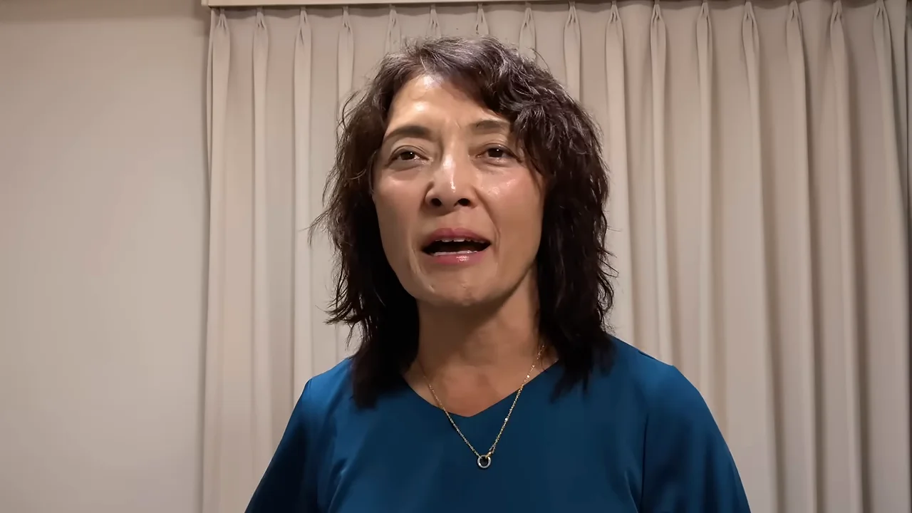 カーテンを背にして正面を向き、口を開けて話す女性