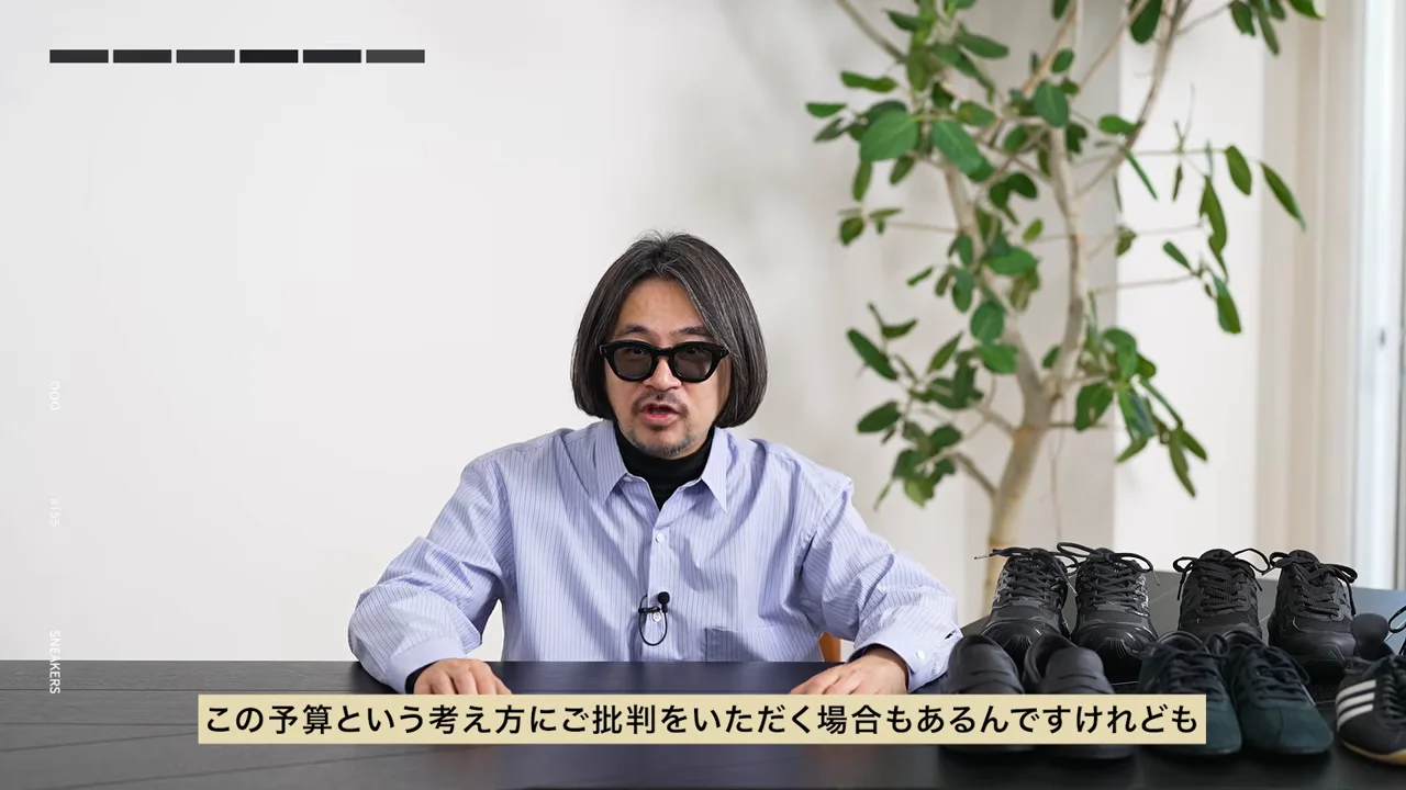 黒いスニーカーを並べた机の前に座る男性が話している様子