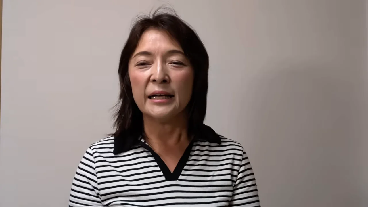 ボーダー柄のシャツを着た女性が正面を見つめながら口を開いて話しています。