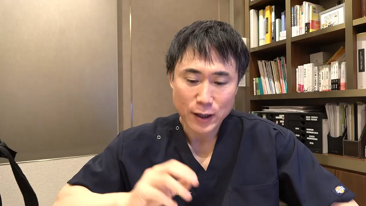 本棚を背にした紺色のスクラブを着た男性が、手振りを交えながら話しています。