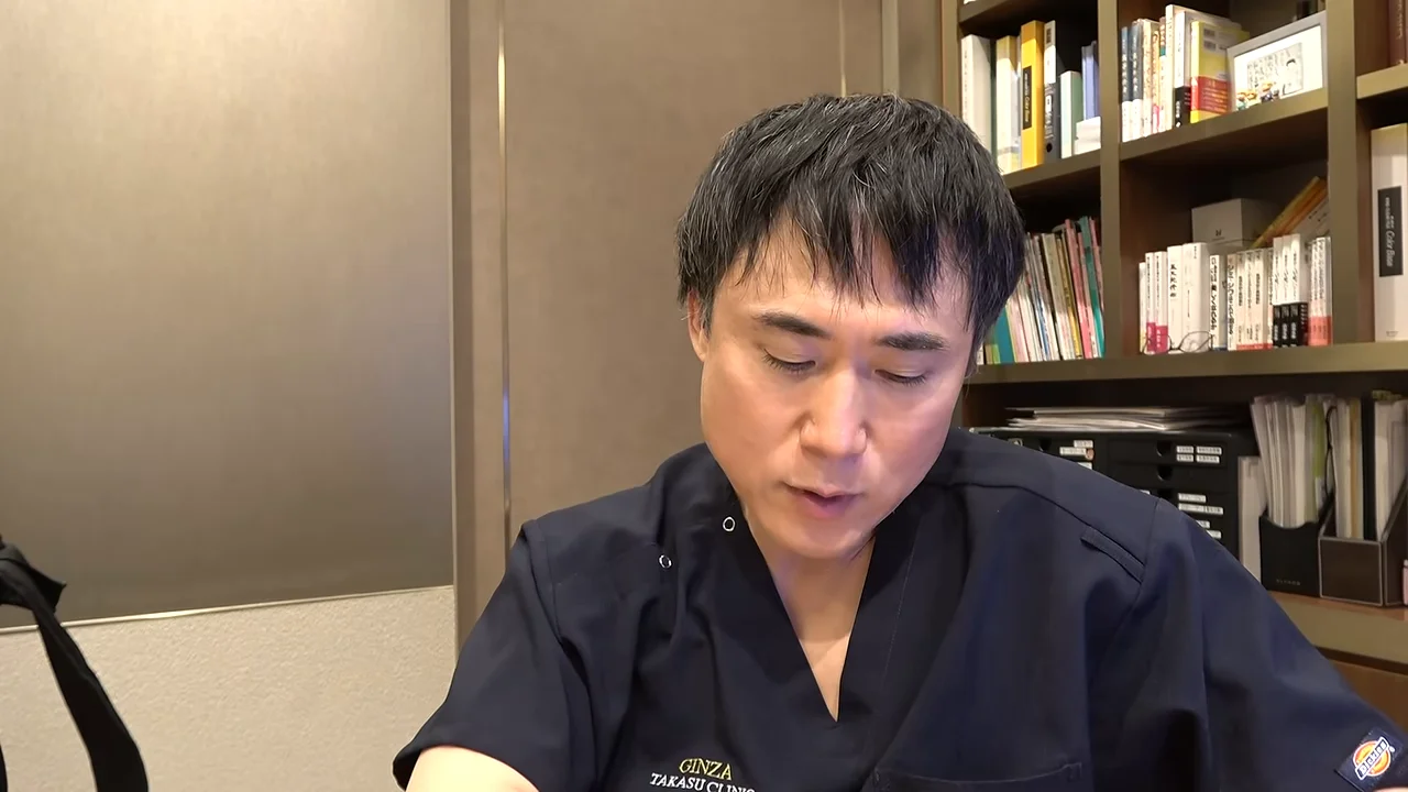 紺色のスクラブを着た男性が、視線を下に向けながら話しています。