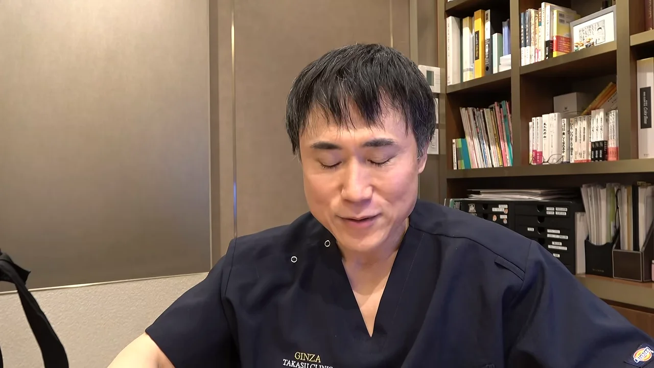 本棚の前に座った男性が、目を細めながら正面に向かって話しています。