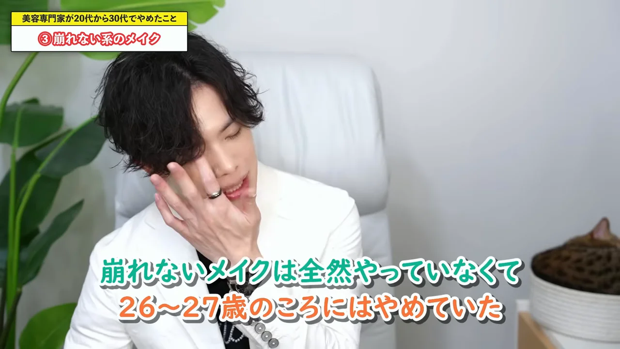 男性が右手を顔に添えながら目を細めて話しています。