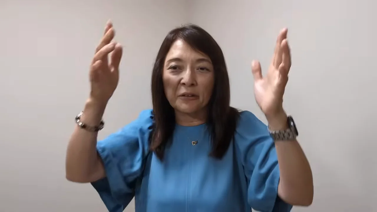 女性が両手を高く掲げて話している。