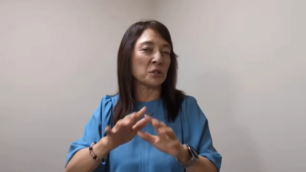 女性が胸の前で手を動かしながら話している。