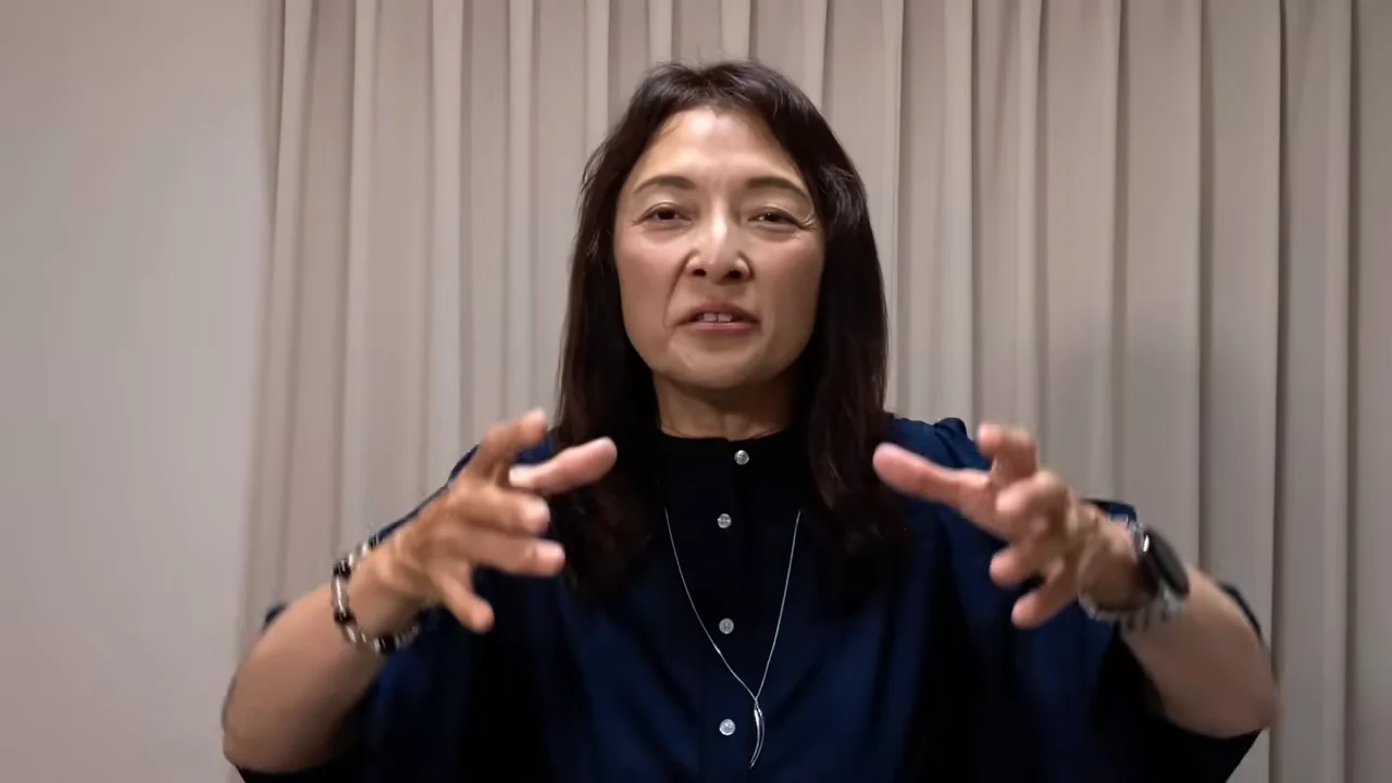 カーテンの前に立つ女性が両手を広げて話している様子。