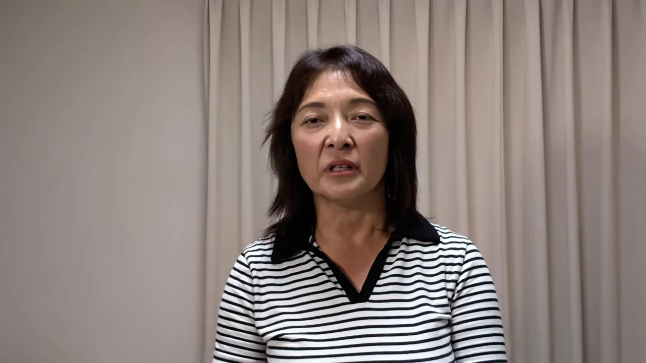 カーテンの前に立つ女性が正面を向いて話を続けています。