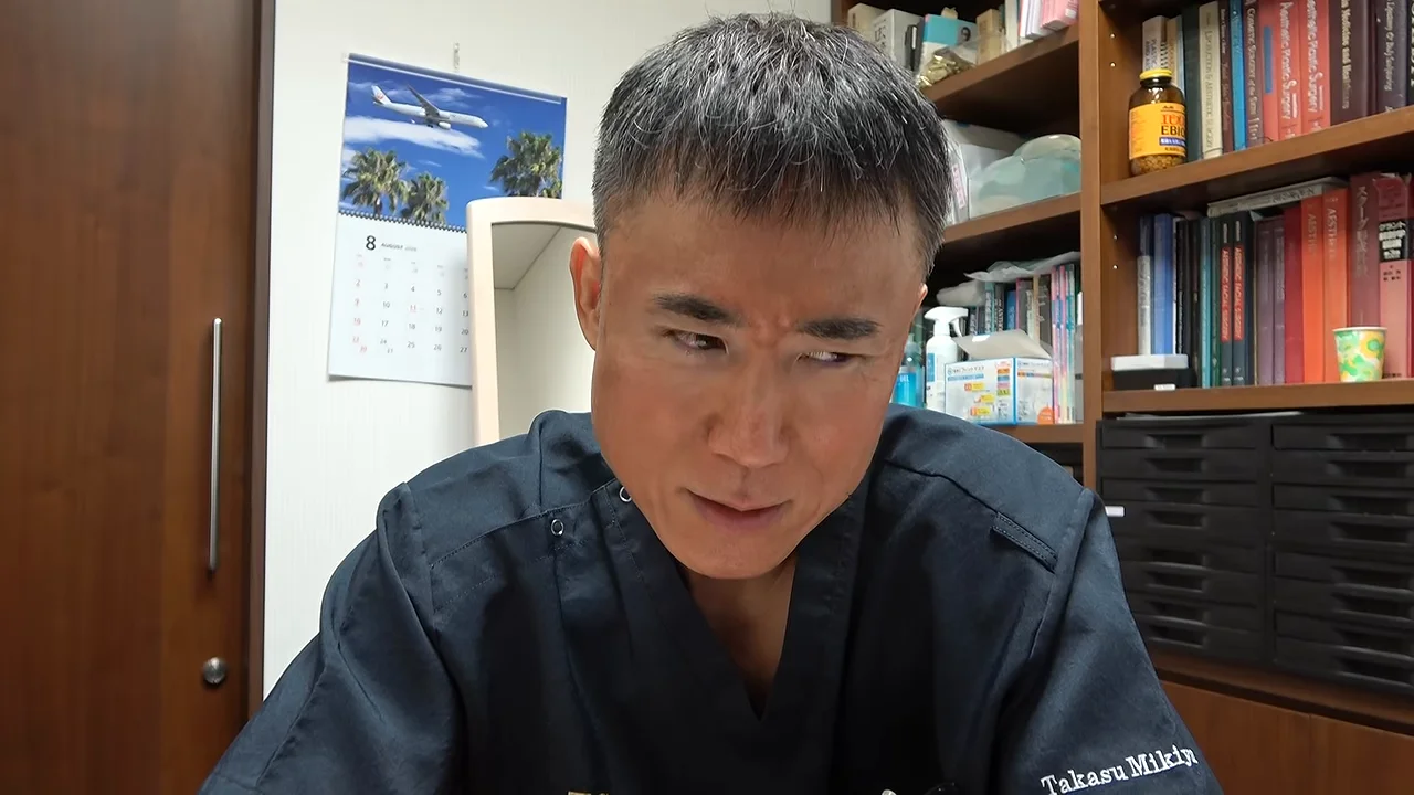 視線をやや下に向けて落ち着いた表情でカメラに向かって話す男性
