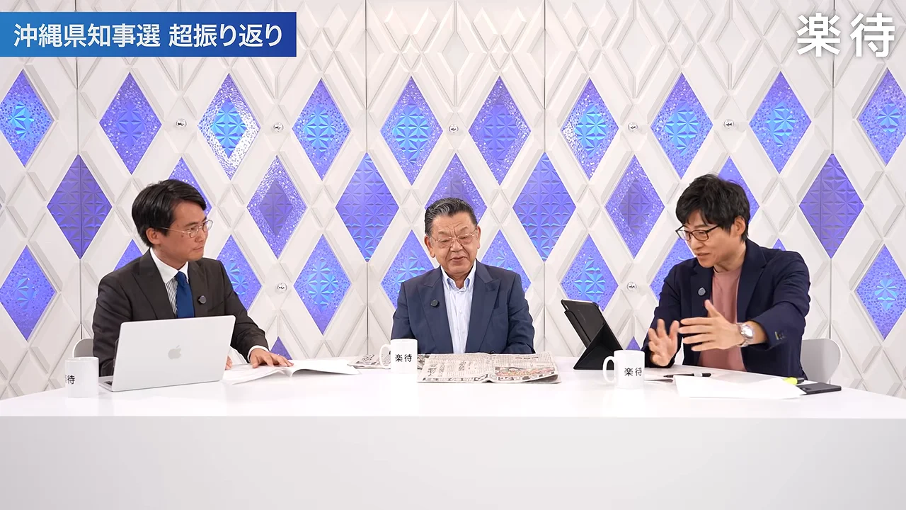 白いテーブルを囲んだ3人の男性がスタジオで議論を行っています。