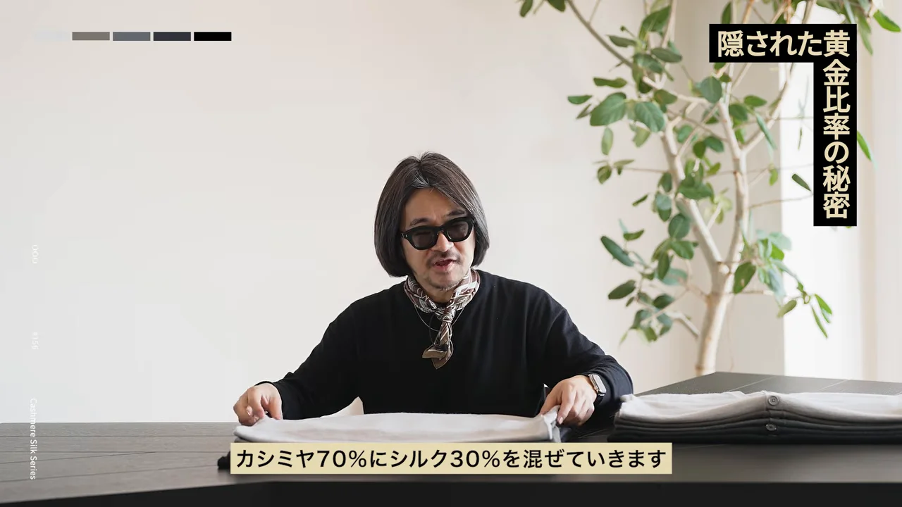 サングラスをかけた人が、テーブルの上の白い衣類に両手を添えている。