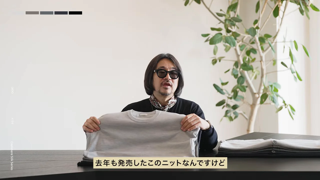 サングラスをかけた人が、淡いグレーのセーターを両手で広げている。