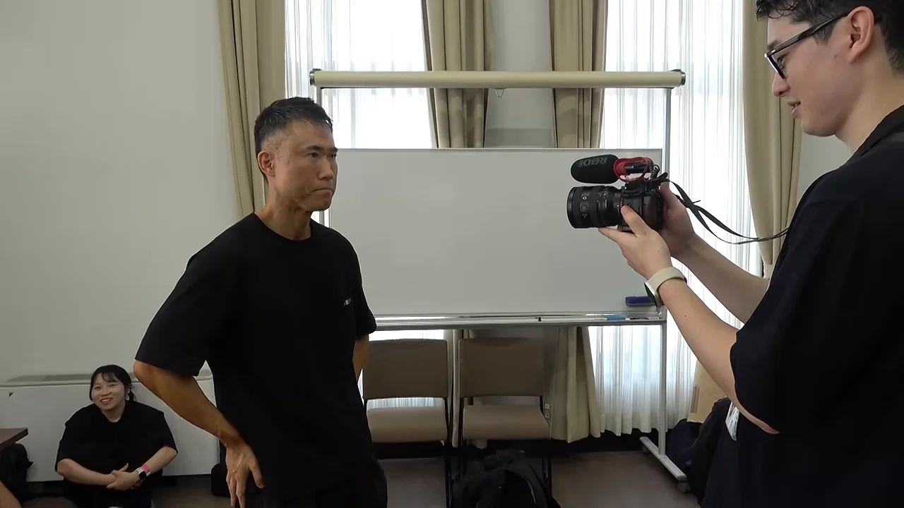 カメラを手にした男性が黒いTシャツの男性を撮影している様子。
