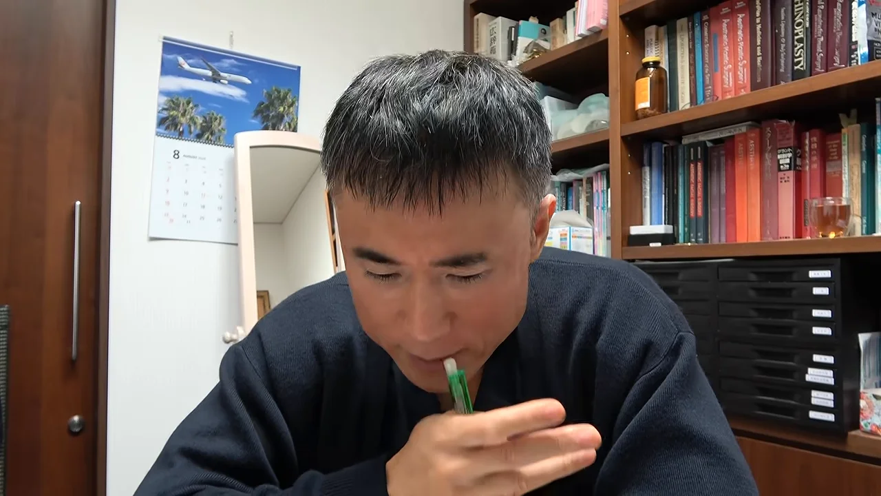 部屋の中でペンを口元に寄せながら話す男性。