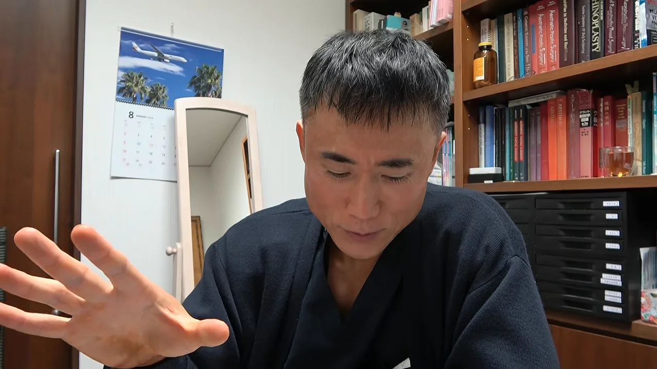 カメラに向かって片手を広げながら話す男性。