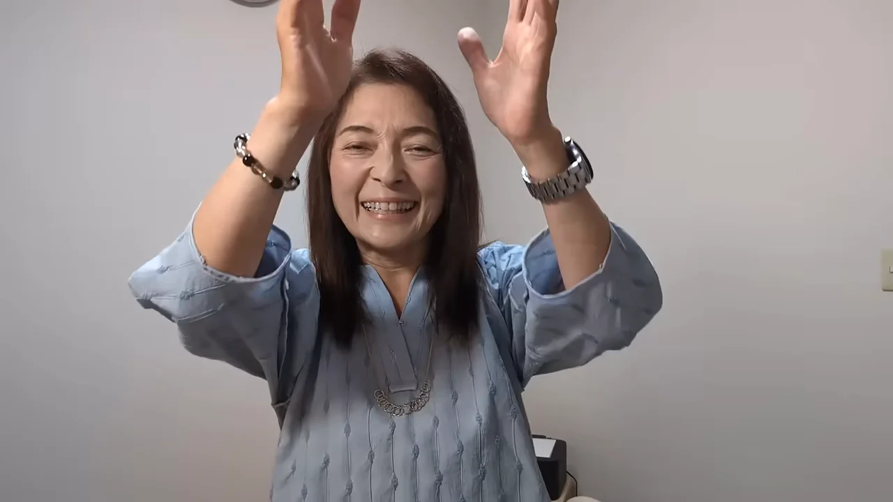 水色の服を着た女性が両手を上げて笑顔を見せている様子。