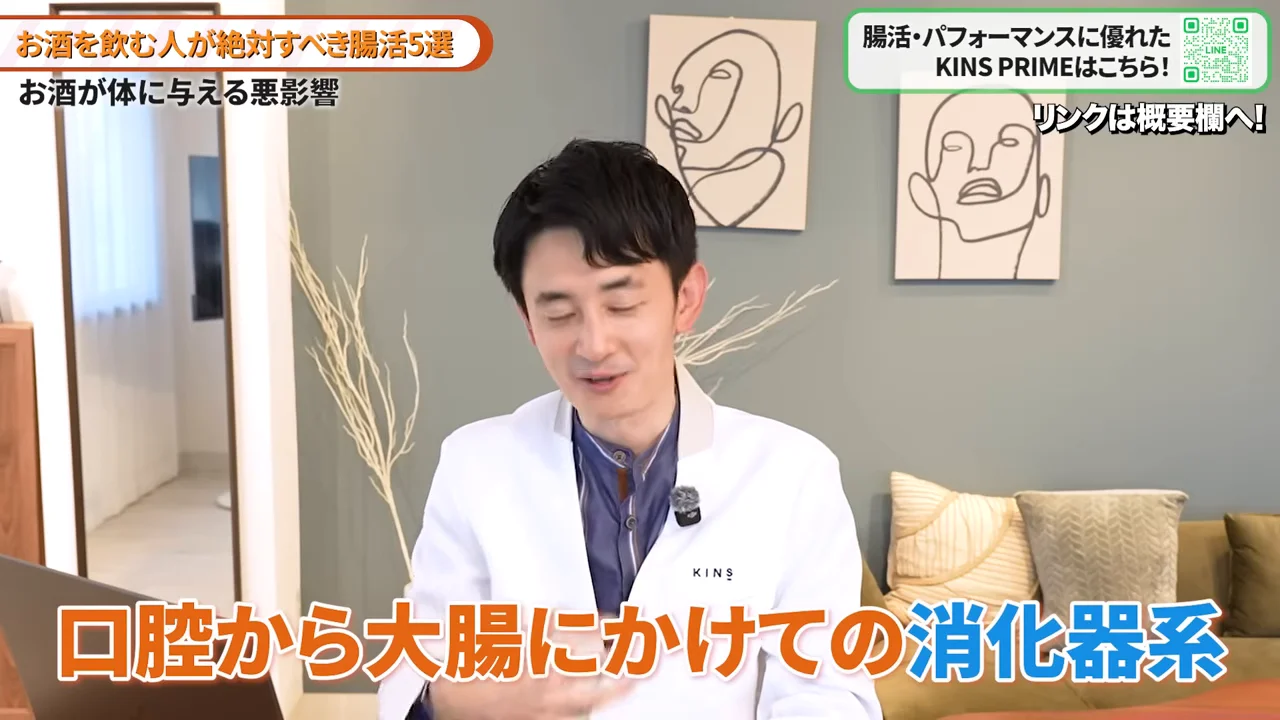 白衣を着た男性が室内で座り、前を向いて話しています。