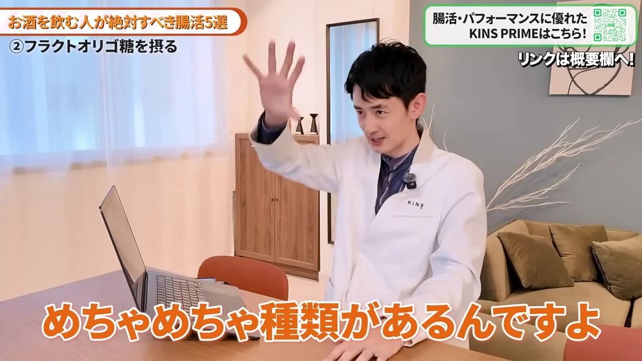 テーブルに座った白衣の男性が、片手を高く挙げながら話しています。