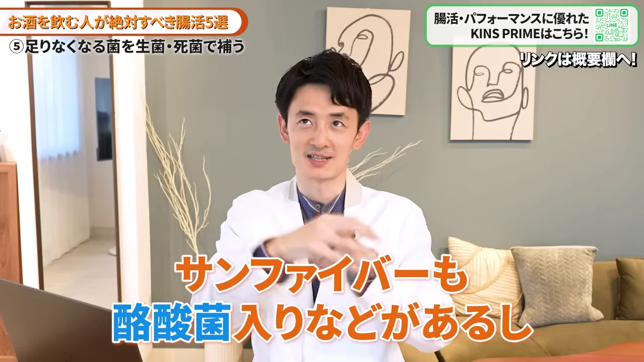 白衣を着た男性が室内で両手を動かしながら話しています。