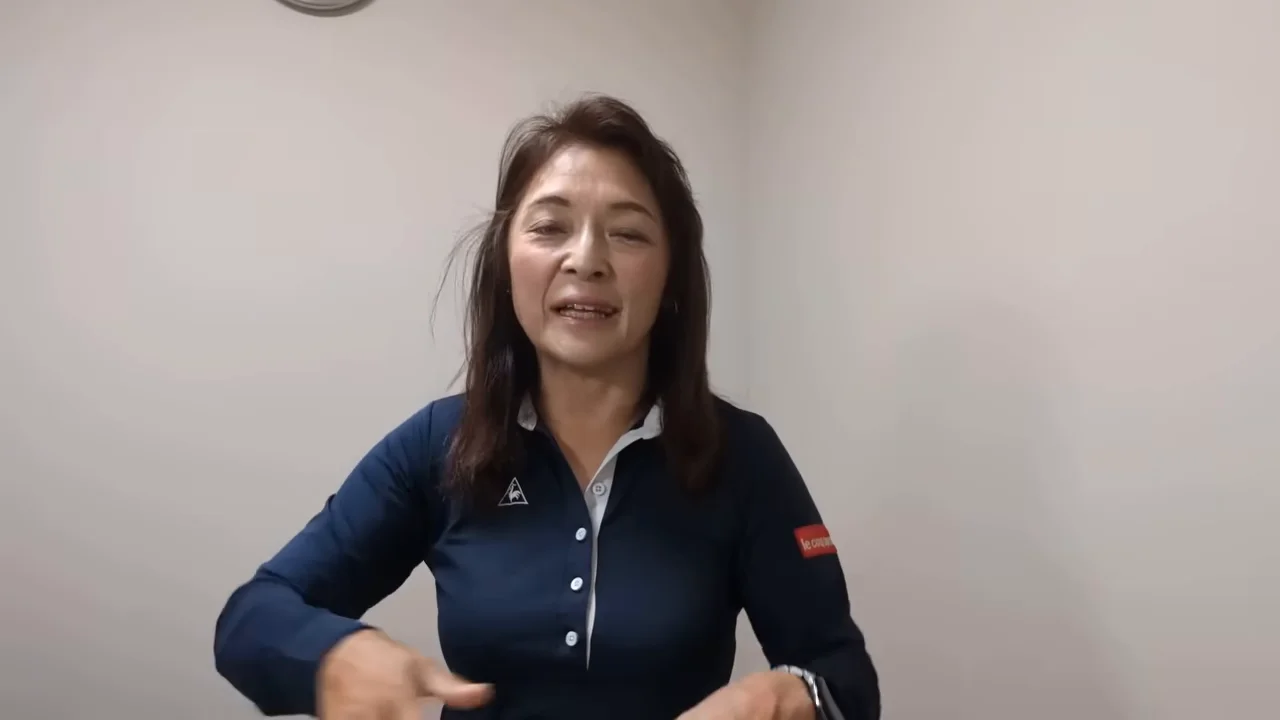 白い壁を背景に紺色のポロシャツを着た女性が話している様子