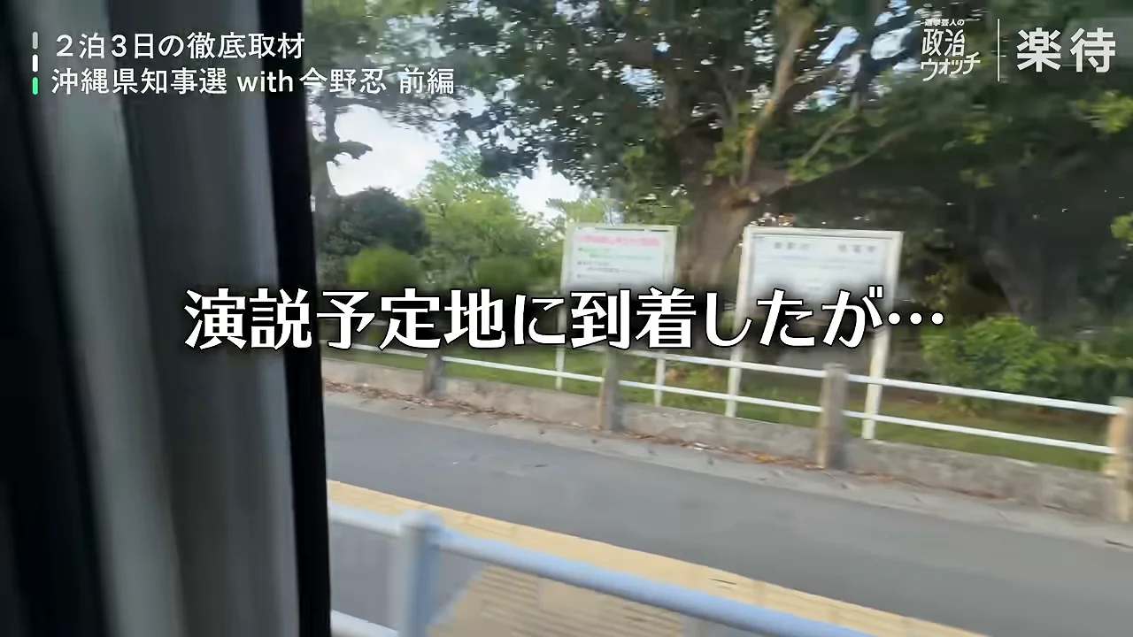 車の窓から見える、木々や看板が並ぶ道路沿いの風景。