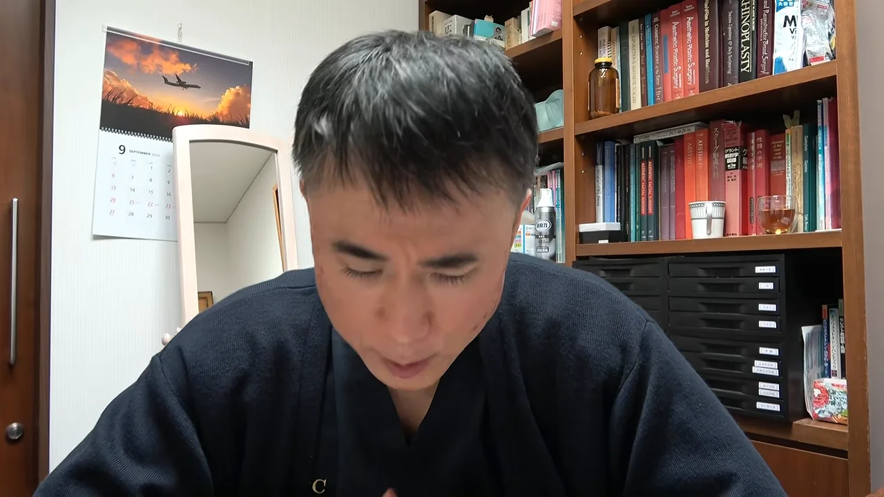 本棚の前に座り、視線を落として話す男性の姿。