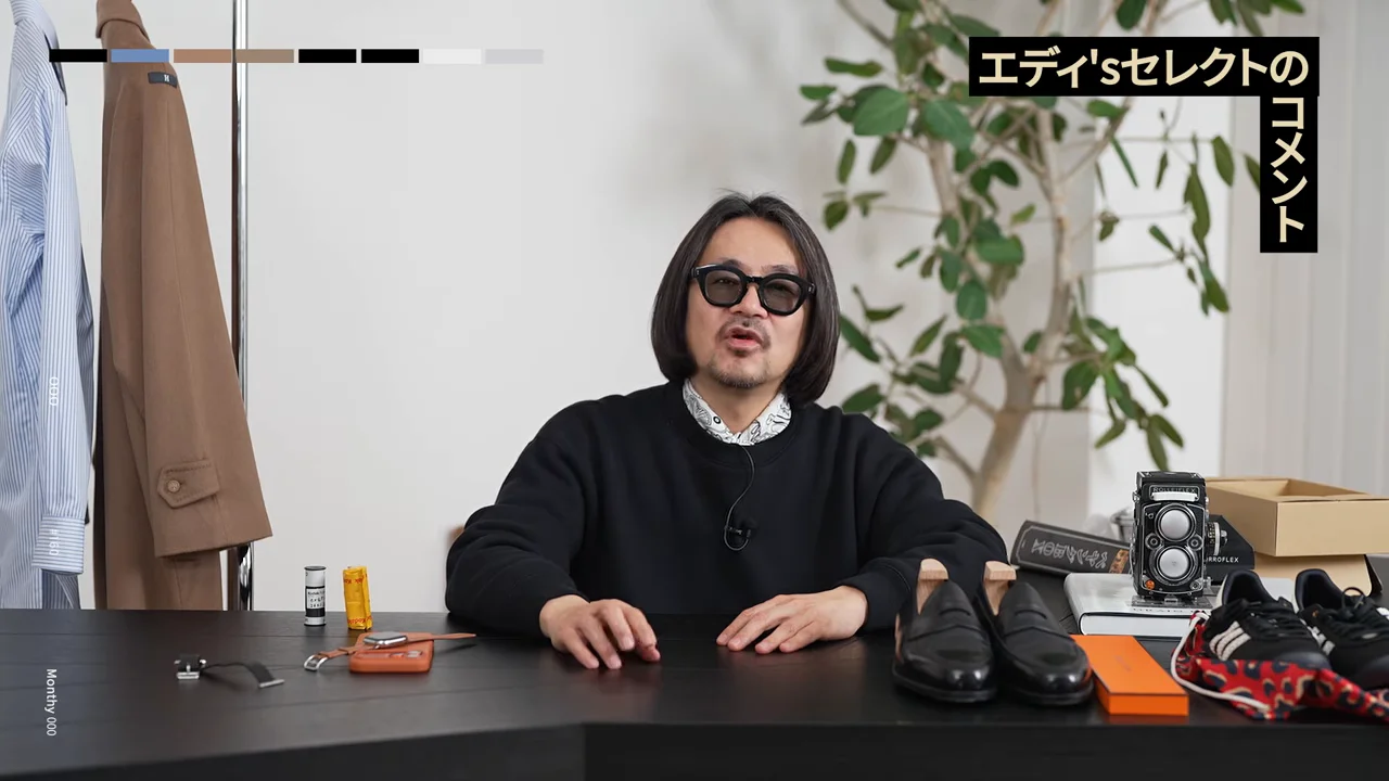 机に並んだ小物の前で身振り手振りを交えながら語る男性