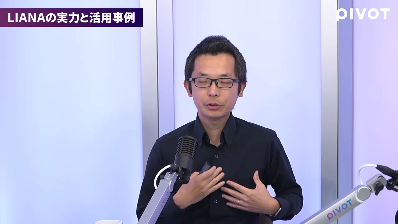 マイクの前に座り、身振りを交えながら話す眼鏡をかけた男性が映っています。