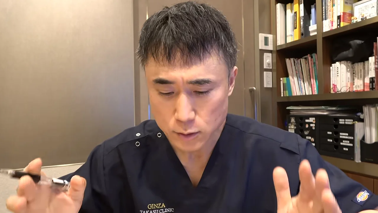 紺色のスクラブを着た男性がペンを持ち、両手を広げて話している様子。