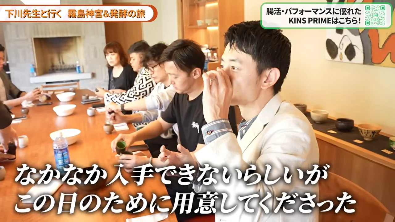 長いテーブルに並んだ人々の中で、手前の男性が器を口元に運んで飲み物を味わっている様子。