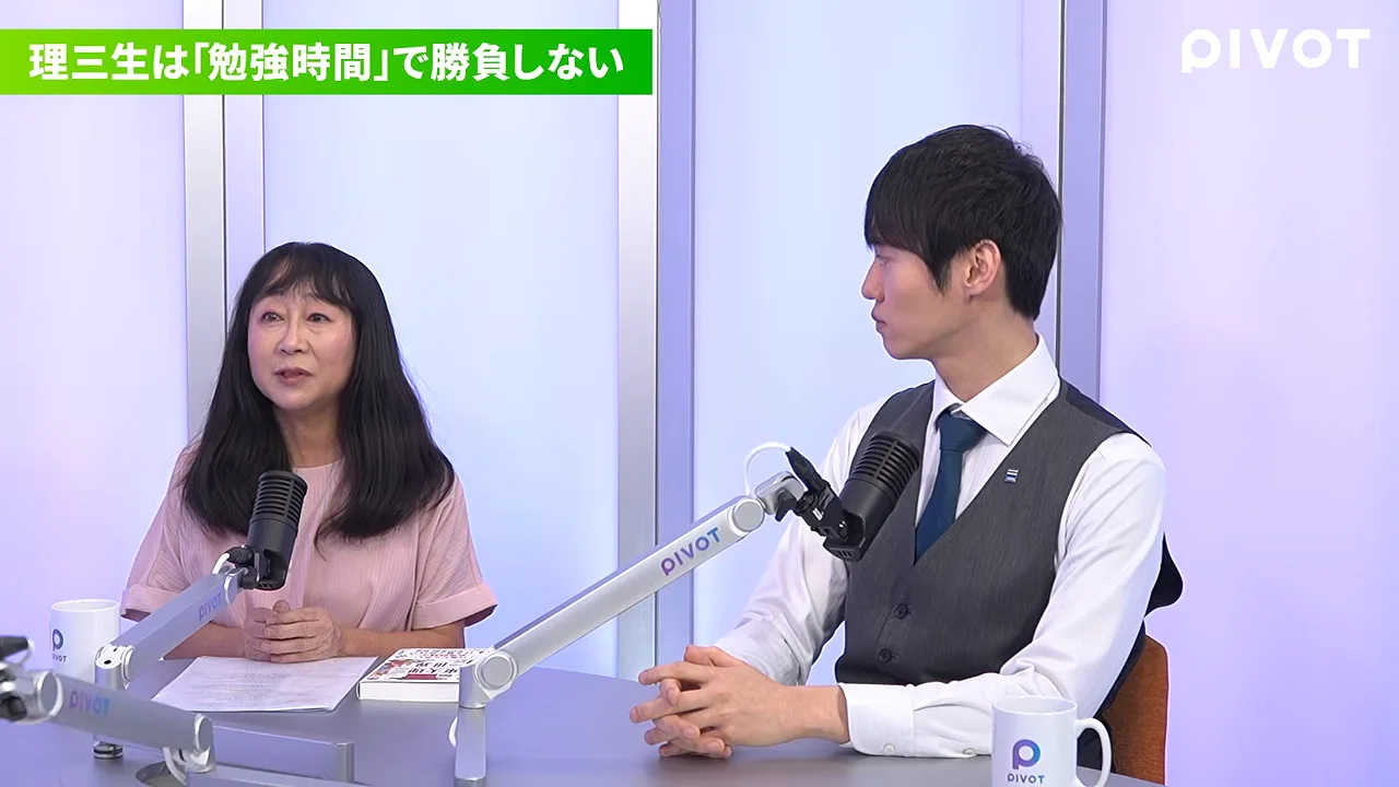 マイクの前で話す女性と、その隣で話に耳を傾けるスーツ姿の男性。