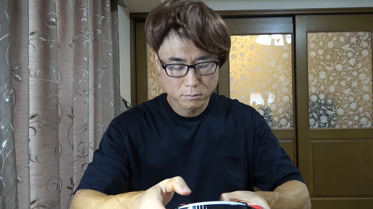 茶色のウィッグと眼鏡をつけた男性が、手元の機器を見下ろしています。