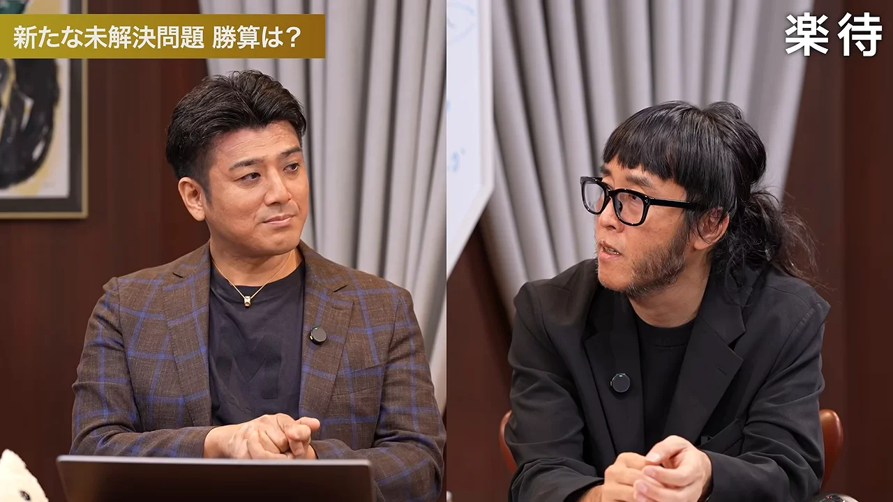 座った男性二人が互いの方を向き、手を組んでいる。