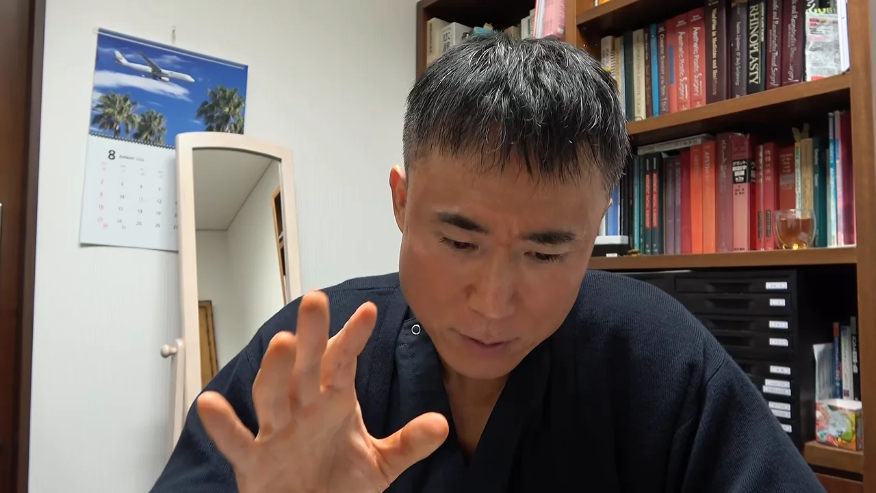 本棚の前に座った男性が右手を前に出しながら話している様子。