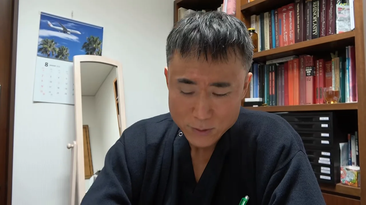 本棚の前に座った男性が下を向きながら話している様子。
