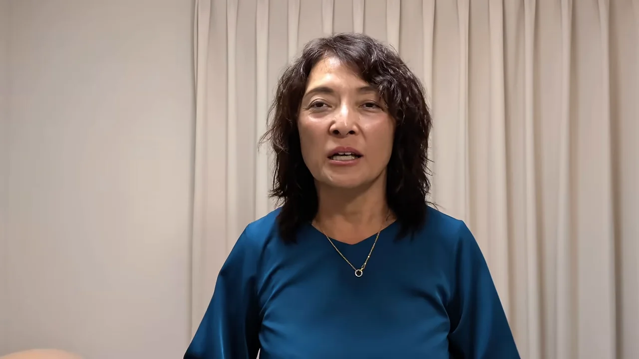 薄い色のカーテンを背景に、青い服を着た女性が話している様子。