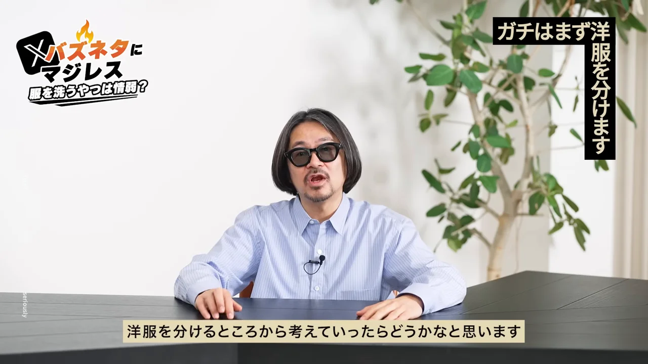 眼鏡をかけた男性が正面を向いて机の前で話している様子。